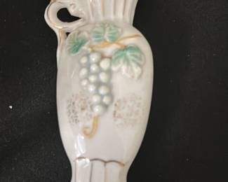 Porcelain Grape Motif Bud Vase — This delicate porcelain bud vase features a raised grape cluster design with green leaves and subtle gold accents. The vase has an elegant, fluted top and a small pedestal base, perfect for holding a single flower or small arrangement. Measuring approximately 5 inches tall, this charming piece adds a vintage touch to your decor. It is in good condition with minor signs of use and no visible chips or cracks. A lovely accent for bedrooms and display cabinets alike.