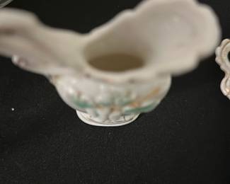 Porcelain Grape Motif Bud Vase — This delicate porcelain bud vase features a raised grape cluster design with green leaves and subtle gold accents. The vase has an elegant, fluted top and a small pedestal base, perfect for holding a single flower or small arrangement. Measuring approximately 5 inches tall, this charming piece adds a vintage touch to your decor. It is in good condition with minor signs of use and no visible chips or cracks. A lovely accent for bedrooms and display cabinets alike.