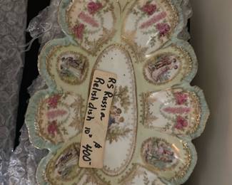 RS Russia Relish Dish Blue Pink Gold — This RS Russia relish dish showcases exquisite craftsmanship with delicate blue, pink, and gold accents. The dish features ornate scalloped edges with intricate floral gold detailing and romantic Victorian-style figures in various oval sections. Measuring approximately 12 inches in length and 8 inches wide, this porcelain piece is decorative and perfect for special occasions or display. It is in good condition with minor wear consistent with age but no visible chips or cracks. The RS Russia maker's mark is present on the bottom, confirming its authenticity and collectible value.