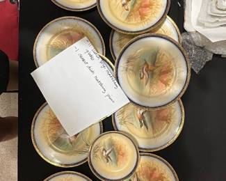 11-Limoges France Duck Plates — This lovely set of Limoges dinnerware from France features hand-painted ducks in a natural marsh scene, bordered with a rich cobalt and gold rim. The set includes 11 lunch size matching plates and 1 dessert dish, each crafted from fine porcelain with exquisite detail and vibrant colors. The plates measure approximately 9.5 inches in diameter, ideal for both display and dining. These plates are in good condition with minor signs of use and no visible chips or cracks. The backstamp confirms their authenticity as Limoges porcelain, a highly regarded maker known for quality French ceramics.