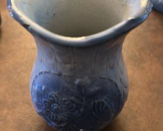 Blue Floral Ceramic Vase — This charming blue ceramic vase features an embossed floral pattern with intricate details. Its unique flared and scalloped rim adds character to this decorative piece, ideal for dining room display or flower arrangements. The vase measures approximately 5 in height and 3.5 in width, making it a perfect accent for small spaces. It is in good condition with minor surface wear consistent with age but no visible chips or cracks. A lovely example of vintage home decor suitable for collectors or daily use.