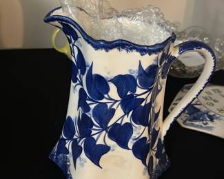 Blue White Floral Ceramic Pitcher — This charming ceramic pitcher features a blue floral leaf design on a white background, showcasing a unique scalloped rim and angular base. Hand-painted details highlight the classic style, while the sturdy handle offers ease of use. Measuring approximately 10 in height, 7 in width, and 5 in depth, this pitcher is perfect for decorative use or serving. It is in good condition with minor surface wear typical of vintage ceramics. The maker’s mark on the bottom reads: "Made by Mrs. Luis Davis, Independence."