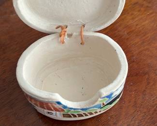 Lucques Mexico Hand-Painted Ceramic Box — This charming Lucques Mexico ceramic box features hand-painted designs of houses and landscapes in vibrant colors. Crafted from glazed ceramic with a natural beige base, it has a hinged lid secured by a small leather cord. Measuring approximately 3.5 inches wide, 2.6 inches tall, and 2.3 inches deep, it fits perfectly as a decorative trinket or jewelry box. The piece is in good condition with minor surface imperfections consistent with handmade ceramics. Signed on the base, this collectible highlights Mexican folk art craftsmanship.