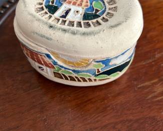 Lucques Mexico Hand-Painted Ceramic Box — This charming Lucques Mexico ceramic box features hand-painted designs of houses and landscapes in vibrant colors. Crafted from glazed ceramic with a natural beige base, it has a hinged lid secured by a small leather cord. Measuring approximately 3.5 inches wide, 2.6 inches tall, and 2.3 inches deep, it fits perfectly as a decorative trinket or jewelry box. The piece is in good condition with minor surface imperfections consistent with handmade ceramics. Signed on the base, this collectible highlights Mexican folk art craftsmanship.
