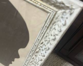 Framed Child Silhouette Portrait — Charming framed silhouette portrait of a child's profile in dark brown on a cream background, presented in an ornate distressed white frame. The piece appears to be paper cut or printed and is mounted behind glass with decorative molded frame detailing. Good size for wall or tabletop display in a nursery, hallway, or gallery wall; frame shows light surface wear consistent with age. Overall condition is good with minor scuffs to frame and slight toning to the paper; ready to hang or display.