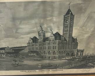 Union Station Nashville Print — Framed lithographic print depicting Union Station, Nashville, Tennessee (terminals of the Nashville, Chattanooga & St. Louis Railway). The piece is matted and set in a simple oak-tone wooden frame with glass, showing architectural detail of the historic station in grayscale. Overall size is moderate and suitable for wall display in a bonus room or office; frame shows light surface wear and the paper has mild age-toning and a small crease near the top edge. Good estate-sale condition for display with no major tears to the image; glass and frame are intact though the frame has minor scuffs consistent with normal use.