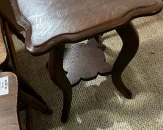 Vintage Wood Side Table — This vintage wooden side table features a scalloped edge square top and curved legs connected by a small ornamental shelf. Constructed from dark-stained wood, it has a compact design suitable for small spaces or as an accent piece. Measuring approximately 20 in height, 16 in width, and 16 in length, this piece is lightweight and easy to move. The table is in good condition with minor surface wear consistent with age. Its timeless style makes it versatile for various décor settings.