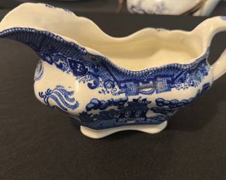 Blue Willow Sch- Vitrious Gravy Boat — This charming blue and white Sch- Vitrious gravy boat features the classic Blue Willow pattern and embossed bison mark with the date 1911. Crafted from ceramic, it displays delicate blue designs and a scalloped rim with a sturdy handle for serving. It measures approximately 3.75 inches in height, 8.5 inches in width, and 4 inches in length, perfect for tabletop use. The piece shows signs of crazing consistent with its age but remains structurally sound and functional. A beautiful early 20th-century collectible from the blue dishes collection, it adds elegance and history to any dining setting.