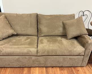Tan Microfiber Sleeper Sofa — This tan microfiber sleeper sofa offers versatile comfort and functionality, making it ideal for basement or guest room use. Upholstered in soft tan microfiber, the sofa includes two matching throw pillows and features a pull-out bed frame underneath for added sleeping space. Measuring approximately 36 inches in height, 78 inches in width, and 36 inches in depth, it provides a compact footprint while maximizing seating and sleeping capacity. The sofa is in good condition with some light signs of use on the cushions but the sleeper mechanism operates smoothly. Its practical design blends well with casual and contemporary interiors.