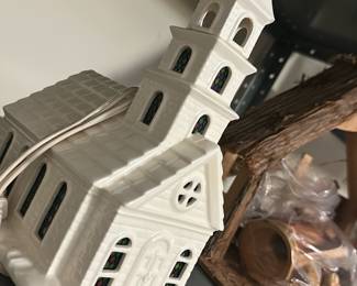 White Ceramic Church Lighted House — Charming white ceramic church-shaped light with molded brick and steeple details and faux stained-glass window inserts. The piece is a plug-in decorative house likely used as a holiday or mantel accent and features an electrical cord for internal illumination. Measures approximately 12 inches tall, 6 inches wide and 6 inches deep — a compact, easy-to-place decoration for shelves or tabletops. In good condition with no visible chips or cracks; cord appears intact though functionality was not tested.