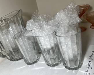 Vintage Glass Pitcher & 6 Glasses — This vintage glass pitcher comes with six matching glasses, each featuring a classic vertical ribbed design. The set is clear and crafted from sturdy glass, making it perfect for serving beverages in style. The pitcher measures approximately 7.5 inches tall and the glasses stand about 5 inches tall. The set is in good condition with no visible chips or cracks and carries sentimental value as it was owned by the seller's great-grandmother.