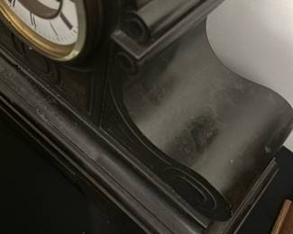 Antique Black marble Mantel Clock — This antique black mantel clock features a curved body with elegant scroll details, showcasing classic early 20th-century design. The clock face has Roman numerals and visible winding holes, framed by a brass bezel with an enamel dial. Measuring approximately 10 in high, 18 in wide, and 6 in deep, this clock is an authentic decorative timepiece ideal for a vintage mantel or shelf. It shows signs of surface wear and dust consistent with age but appears structurally sound. This piece is a fine example of traditional clockmaking, adding nostalgic charm to any bedroom or living room setting.