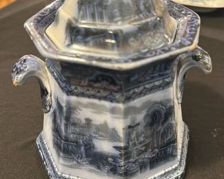 Wadams Blue Athens Covered Jar — This elegant Wadams covered jar features a classic blue and white transferware design depicting scenes of Athens. The hexagonal form and ornate handles highlight its refined craftsmanship, making it a charming decorative piece or collectible. The jar measures approximately 7 inches tall and 5 inches wide, perfect for display in any home collection. It is in good vintage condition with minor wear consistent with age, including a small chip on the lid rim. The piece bears the Wadams maker's mark and pattern number 36976, indicating its origin and authenticity.