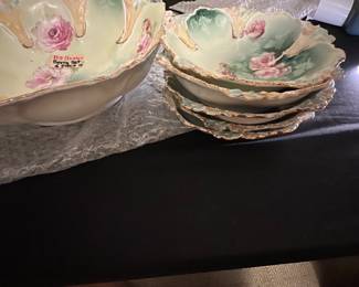 6 pc RS Prussia Handpainted Bowl Set — This beautiful RS Prussia bowl set features handpainted pink roses on a soft green and cream background with ornate scalloped edges. The set includes a large bowl and several smaller matching bowls, each showing delicate floral detail and gold trim. The large bowl measures approximately 12 in in diameter and the smaller bowls about 7 in. These pieces are in good condition with minor wear consistent with their age, showcasing elegant late 19th to early 20th-century porcelain craftsmanship. A charming addition to any vintage ceramic or china collection.