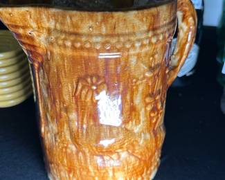 Vintage Brown Glazed Ceramic Pitcher — This vintage ceramic pitcher features a rich brown glaze with a textured surface and an artisan-crafted handle. The pitcher displays a rustic charm with marks of age and a beautiful crackle glaze pattern throughout. Measuring approximately 6 inches tall and 4 in diameter, it's a lovely decorative piece for any kitchen or dining display. The item is in good condition with minor imperfections consistent with vintage pottery. Its handmade quality and distinctive glaze make it a unique collectible for ceramic enthusiasts.
