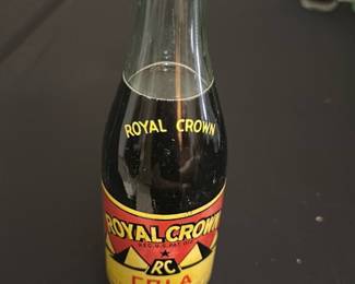 Royal Crown Cola Vintage Glass Bottle — This vintage Royal Crown Cola glass bottle features classic branding with a red and yellow label and the iconic RC logo. The bottle has the traditional shape of mid-20th century soda bottles, complete with a metal cap and embossed lettering on the neck. Measuring approximately 7.5 inches tall, it is a collectible item perfect for soda enthusiasts or vintage collectors. The bottle is in good condition with minimal wear visible on the label and no apparent cracks or chips. A great nostalgic piece representing American soda history.