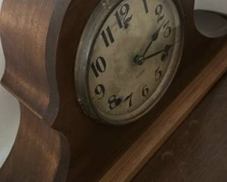 Gilbert Vintage Wooden Mantel Clock — This charming Gilbert vintage wooden mantel clock features a classic tambour style with smooth curved edges. The clock face shows aged patina with bold black numerals and the Gilbert brand mark visible. Measuring approximately 9 inches tall, 17 inches wide, and 5 inches deep, this clock is designed for display on a mantel or shelf. The wood casing exhibits some wear consistent with age but remains structurally sound. A fine example of early 20th-century American clockmaking, it adds vintage character to any room.