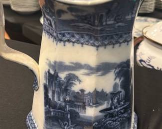 Adams & Co. Blue Transferware Pitcher — This elegant Adams & Co. blue transferware pitcher features a picturesque landscape scene framed by intricate border patterns. Crafted from fine ceramic with a distinctive octagonal shape, this pitcher showcases classic 19th-century English ceramic artistry. Standing approximately 8 inches tall and 6 inches wide at its base, it is a perfect decorative or functional piece. The pitcher is in good vintage condition with typical crazing and minor wear consistent with its age. Marked with the Adams & Co. Athens pattern and model number 6978, it represents collectible English transferware from a respected maker.