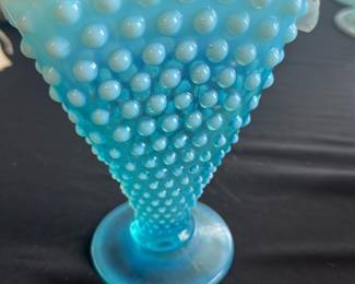 Fenton Blue Hobnail Opalescent Vase — This charming Fenton blue hobnail opalescent vase stands 6 inches tall and features a distinctive hobnail pattern with a flared, ruffled rim. Crafted with opalescent glass, this vintage piece adds a delicate and collectible touch to any room. The vase measures approximately 6 inches in height and has a stable round base. It is in good condition with no visible chips or cracks, though some minor surface wear may be present consistent with age. A classic example of Fenton's artisan glasswork, perfect for collectors or vintage decor enthusiasts.