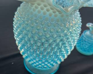 Blue Hobnail Vase with Ruffled Edge — This charming blue hobnail vase features a classic ruffled edge and textured body, characteristic of vintage hobnail glass designs. Made from opalescent glass, it showcases a beautiful gradient from blue to frosted white at the ruffled rim. The vase measures approximately 7 inches in height and 5 inches in width, making it an ideal decorative piece for a bedroom or living area. It is in good condition with no visible chips or cracks, showing minor surface wear consistent with age. This hobnail vase is a collectible piece that adds a touch of nostalgic charm to any collection or display.
