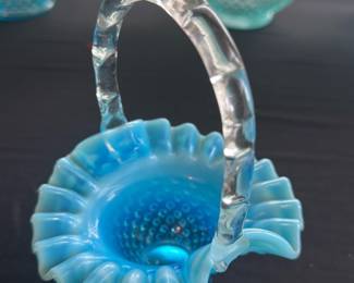 Blue Hobnail Glass Basket — This charming blue hobnail glass basket features a clear twisted handle and ruffled edges that highlight its delicate craftsmanship. The basket is made of vibrant blue glass with a textured hobnail pattern, creating a striking visual appeal. Measuring approximately 6 inches tall with a width of 4.5 inches and a length of 5 inches, it is perfect for decorative display. The glass is in excellent condition with no chips or cracks visible. This piece makes a lovely vintage collectible or accent decor item for any home.