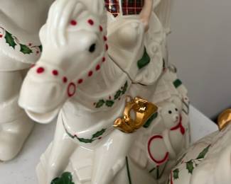 Lenox Elf Rocking Horse Teapot — This charming Lenox Holiday Elf and Rocking Horse Teapot is a festive addition to any Christmas decor. Crafted from fine porcelain, it features a detailed elf figure riding a white rocking horse adorned with holly, gold accents, and a teddy bear motif. The teapot measures approximately 7 inches tall, 9 inches wide, and 5 inches deep, making it a delightful centerpiece for holiday gatherings. It is in excellent condition with no chips, cracks, or visible wear, and includes its original packaging. A collectible piece from Lenox's For The Holidays series, perfect for adding whimsical charm to your seasonal table.