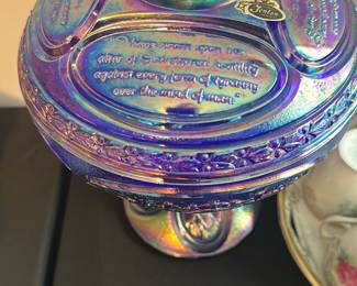 Fenton Blue Carnival Glass Eagle Covered — This striking Fenton covered dish features iridescent blue carnival glass with an eagle finial on top. The lid is embossed with inspirational text and the iconic Fenton sticker is present, confirming authenticity. The piece stands approximately 9 inches tall and 7 inches wide, making it an eye-catching collectible centerpiece. The dish is in excellent condition with vibrant coloration and no chips or cracks. A rare Fenton collectible, perfect for carnival glass enthusiasts or patriotic decor collectors.