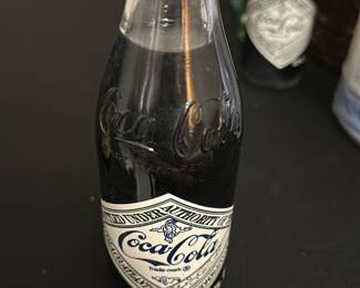 Coca-Cola 75th Anniversary Bottle — Celebrate Coca-Cola's 75th anniversary with this vintage collectible bottle commemorating the first bottler's contract in Nashville from 1900 to 1975. The glass soda bottle features the classic Coca-Cola branding with an embossed logo and special 75th anniversary label. Measuring approximately 7 inches tall, this unopened bottle is in good condition with minor wear on the label and cap. A great addition for Coca-Cola collectors and vintage soda enthusiasts. The bottle carries nostalgic value and is a unique piece of beverage history.