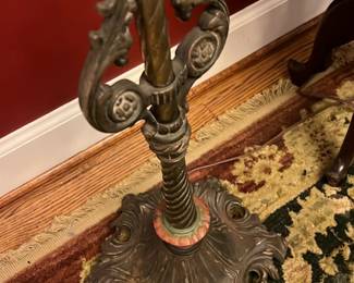 Vintage Brass Floor Lamp w/ Fringe Shade — This vintage brass floor lamp features an ornate twisted pole and elaborately designed base with intricate floral details. The cream fabric lampshade is adorned with subtle floral patterns and a decorative fringe trim, adding a touch of classic elegance. Standing approximately 59 inches tall, this lamp complements traditional or antique-style interiors perfectly. It retains good condition with minor wear consistent with age, enhancing its character and charm. A beautiful addition to any front room décor, this lamp brings both style and warmth.