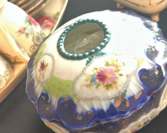 Antique Floral Porcelain Hair Receiver — This antique floral porcelain hair receiver is a charming and rare collectible from the master bedroom collection. Featuring delicate hand-painted pink and yellow flowers on a white background with rich cobalt blue and green accents, it showcases fine craftsmanship. It measures approximately 3.5 inches in height and 5 inches in diameter, making it a compact yet elegant decorative piece. The hair receiver is in good condition with minimal wear typical of its age and retains most of its original detailing and paint. A unique and graceful addition for collectors of vintage bedroom accessories.