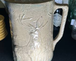 Vintage Ceramic Deer Pitcher — This vintage ceramic pitcher features an embossed deer motif with intricate detailing around the body. Crafted from glazed ceramic in a muted cream color, it has a sturdy handle and a spout for easy pouring. Measures approximately 8 in tall, 6 in wide, and 5 in deep, making it a practical and decorative piece. The pitcher is in good condition with minor surface wear consistent with age but no visible cracks or chips. Ideal as a collectible or for rustic home decor display.
