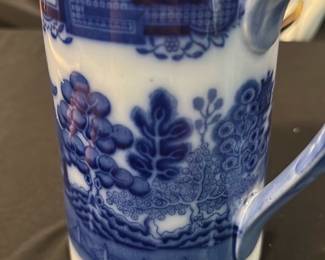 Burslem England Blue Willow Pitcher — This charming Burslem England pitcher features the classic Blue Willow pattern, renowned for its intricate blue and white design. Crafted from fine porcelain, it includes a fitted lid and a gracefully curved spout and handle, perfect for serving beverages. The pitcher measures approximately 6 inches tall and 4 inches wide, making it a compact and elegant addition to any collection or table setting. It is in good condition with minor signs of use consistent with age and no visible chips or cracks. Marked with the Burslem England hallmark and the Blue Willow stamp, this piece reflects traditional English ceramic craftsmanship.