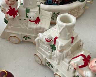 Set(2) Ceramic Train Candle Holder — These charming holiday ceramic train candle holders feature festive details including holly accents, teddy bears, and gift-wielding figures in green and red. Each piece is crafted from white ceramic with hand-painted highlights that evoke classic Christmas decor. The trains are designed to hold taper candles snugly, making them perfect seasonal tabletop accents. Both candle holders are in good condition with minor signs of use but no chips or cracks. Ideal for adding a nostalgic and whimsical touch to holiday decorating.