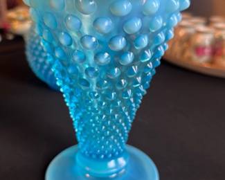 Blue Hobnail Ruffled Edge Vase — This striking blue hobnail glass vase features a distinctive ruffled edge with an opalescent finish that highlights its exquisite craftsmanship. The textured hobnail pattern adds elegance and tactile interest to this decorative piece. Measuring approximately 9 in height and 6 in across the widest ruffled opening, it serves as a beautiful accent for any master bedroom décor. The vase is in excellent condition with no chips, cracks, or damage observed. Its vintage style makes it perfect for collectors or as a statement home décor item.