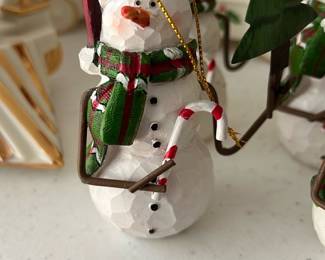 Set(4) Snowman Christmas Ornament — This charming carved wood snowman ornament features a red hat, green plaid scarf, and a festive candy cane in hand. Detailed with hand-painted accents and holding a green pine tree, it embodies classic holiday spirit. Measuring approximately 4.5 inches tall, it is lightweight and perfect for decorating Christmas trees or holiday displays. The ornament is in excellent condition with no visible chips or damage. A timeless holiday collectible, ideal for adding warmth and charm to seasonal decor.
