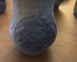 Blue Floral Pottery Pitcher — This charming blue floral pottery pitcher features an intricate embossed flower design on its exterior. The piece has a gracefully flared rim and sturdy handle, ideal for decorative or functional use in the dining room. It measures approximately 5.5 inches in height, 3.5 inches in width, and 4 inches in length, making it a compact yet elegant addition. The pitcher is in good condition, showing some wear consistent with age but no significant damage. Its classic style and glazing suggest it would complement vintage or home decor collections.