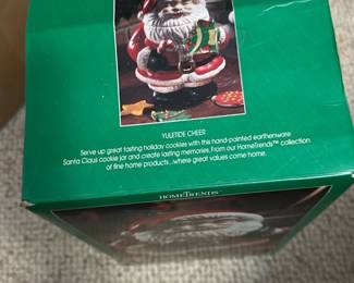 HomeTrends Green Santa Cookie Jar — This HomeTrends hand-painted earthenware Santa Claus cookie jar is a festive holiday piece from the blue dishes room. The green box shows the red-and-white Santa cookie jar with painted details and removable lid, made of earthenware and intended for serving cookies or seasonal display. Boxed item; overall footprint is compact for countertop or mantel display. Item appears in good condition in original packaging with minor shelf wear to the box.