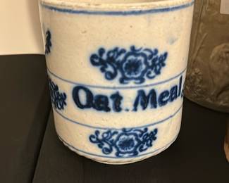 Antique Blue & White Oak Meal Crock — This antique oak meal crock features a classic blue and white glazed stoneware design with decorative floral motifs. It bears the bold text 'Oat Meal' encircling the piece, indicating its original use for oat storage. The crock measures approximately 6 inches in height and 5.5 inches in diameter, making it a charming and functional collectible. It is in good condition with minor surface crazing consistent with age and no visible cracks or chips. A beautiful example of early kitchenware, perfect for vintage collectors or rustic home decor.