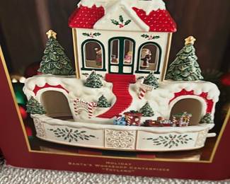 Lenox Santa's Workshop “Toyland” — This festive Holiday Santa's Workshop Centerpiece captures the charm of a snow-covered Christmas village with detailed red roofs, holly accents, and festive trees. The ceramic piece features a circular train track with a colorful toy train, surrounded by candy cane signs and wrapped presents, perfect for holiday décor. Measuring approximately 8 inches tall and 10 inches wide, it is a delightful and eye-catching addition to any holiday setting. The item is in excellent condition with no visible chips or cracks. Its classic holiday theme makes it ideal as a centerpiece or collector's piece for Christmas enthusiasts.