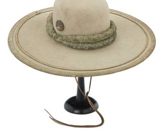 34 An early Mexican Chinaco sombrero Circa 1865 Interior band stamped in gold: Bartley Hats [three crowns]; with multiple further oval dark stamps: [illegible] Almacen The beige fur felt low rounded crown hat with 5 1/2 inch flat brim, padded fabric double band and metal thread wrapped buttons, the edges with wide silver metal thread ribbon edging and braid accents, with interior leather sweat band and leather laces 5.5" H x 17.5" W x 18.75" H; Inner band: 22.25" C Estimate: $2,000 - $3,000