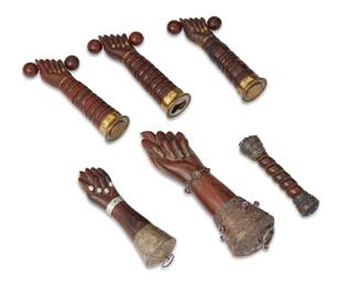 21 A group of South American carved wood talismanic charms 20th century Two with applied Chilean coin: Republica de Chile / [eagle] The group of charms comprising two Brazilian Mano Figas depicting the thumb placed between the index and middle fingers as a gesture to ward off the evil eye of Satan, each mounted with decorative mixed metals, one embellished with lavender-toned semi-precious stones and a bracelet; three fists clenching barbells with gilt metal mounts, and one twisted cylindrical charm with silver mounts 6 pieces Largest: 8.25" L; Smallest: 5.25" L Estimate: $400 - $600