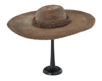 36 An early Mexican sombrero Circa 1860 The pale brown-toned wide brimmed round hat with a low tapered flat crown, likely woven of palm straw, with an added double plaited leather corded band covered with leather strips 3.5" H x 19.75" Dia.; Interior: 21.5" Dia. Estimate: $1,000 - $1,500