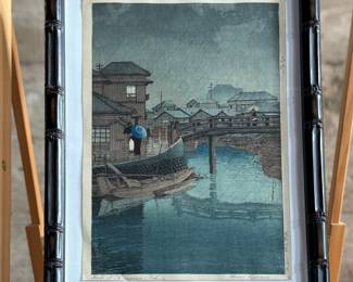 “Rainy Season at Ryoshimachi, Shinagawa”, an original Japanese woodblock print by listed artist, Kawase Hasui. Hand signed circa 1931 and professionally framed. This piece measures (without frame), 15” H x 10.25” W. Kawase Hasui (1883–1957) was the foremost landscape artist of the shin-hanga (“new prints”) movement. Renowned for his serene, atmospheric scenes of snow, rain, and moonlight, he designed approximately 620 woodblock prints over his 40-year career. In 1956, the Japanese government honored him as a Living National Treasure. $2,000 reserve.