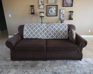 Brown rolled-arm sofa. Skirted base. Includes decorative throw and accent pillow.