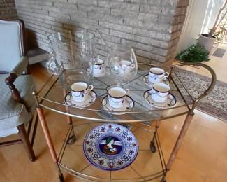 Bar cart with antique cups and saucers, glass wine cooler, decorative hanging plate
