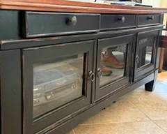 Wooden entertainment center with three drawers and three glass front doors.