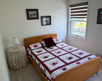 Full sized bed with Amish made quilt, pictures, lamp and table.