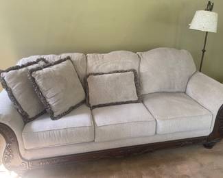 sofa features a light-colored polyester chenille fabric and ornate, carved espresso-finished wood legs and trim, plus matching pillows