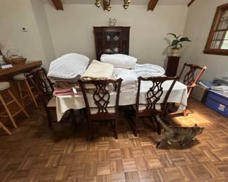 Dining Table with Chairs and Linens - A wooden dining table surrounded by chairs, topped with various linens and blankets. Ideal for family gatherings or as a decorative piece.
