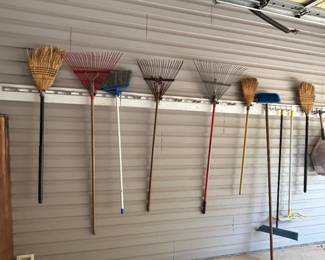 Assorted Brooms and Rakes - A collection of various brooms and rakes for yard and home use, ideal for cleaning and gardening tasks.